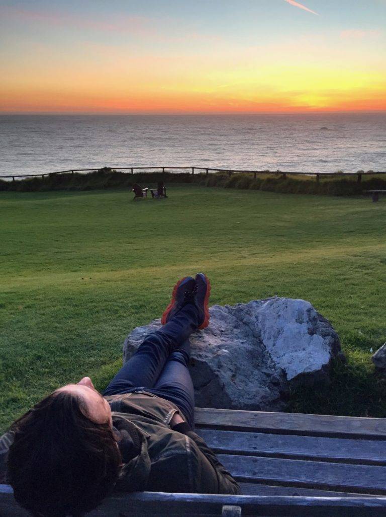 Woman laying on a bench, feet up a rock, enjoying the natural beauty of the sunset